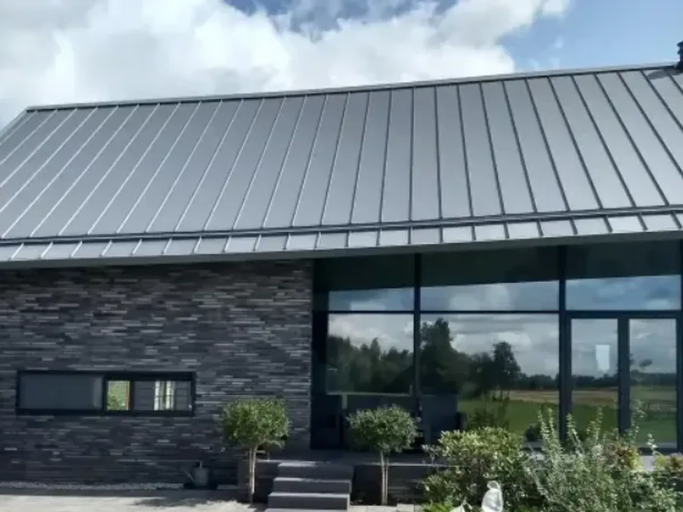 Grijs klikfels-dak boven een woonkamer met grote glaspuien